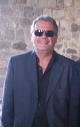 Antonio Giansante in giacca scura e occhiali da sole, davanti a una parete in pietra.